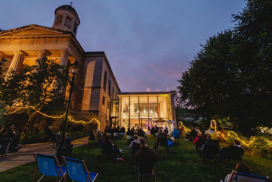 the outside of st george's at night, with people sitting in the garden in lounge chairs